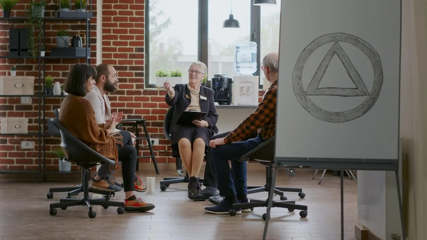 Individuals meet with a psychiatrist to discuss recovery during an AA group therapy session. Patients sit in a circle, talking about addiction with the therapist as part of a rehabilitation program.